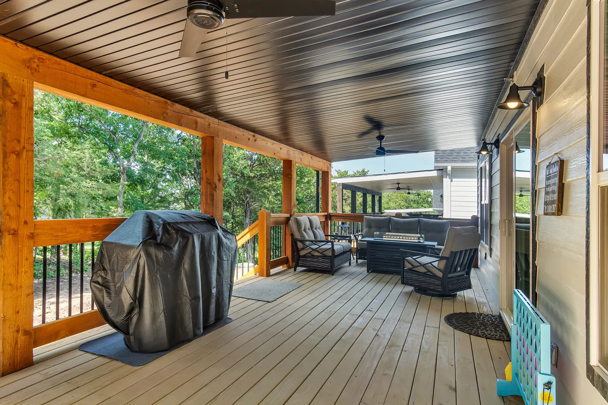A wooden deck with comfortable outdoor seating, a grill, and a classic wooden railing overlooking a serene landscape. The area welcomes both lively barbecues and peaceful coffee mornings.