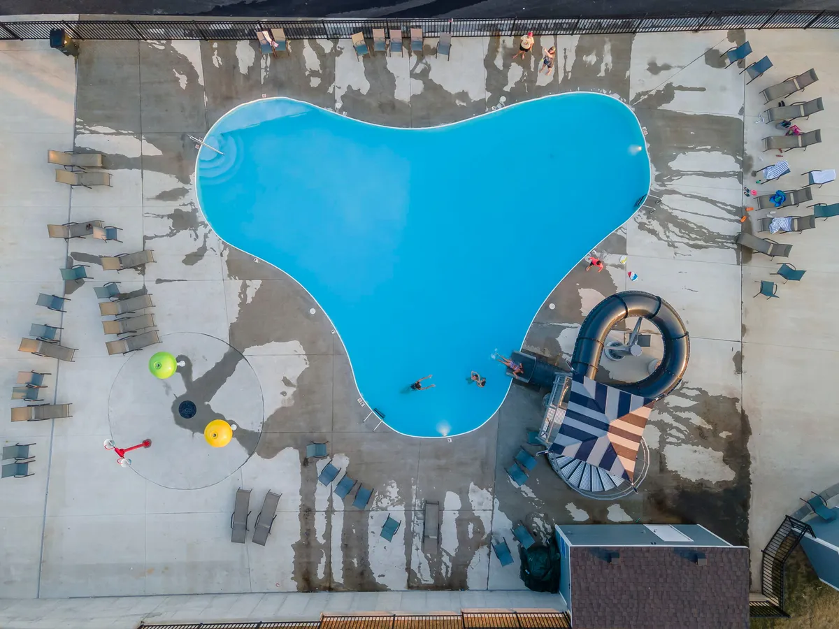 A vibrant outdoor pool area with a water slide, lounge chairs, and a play area filled with colorful balls. Families and children enjoy swimming and splashing under the sun, creating a joyful and energetic summer vibe.