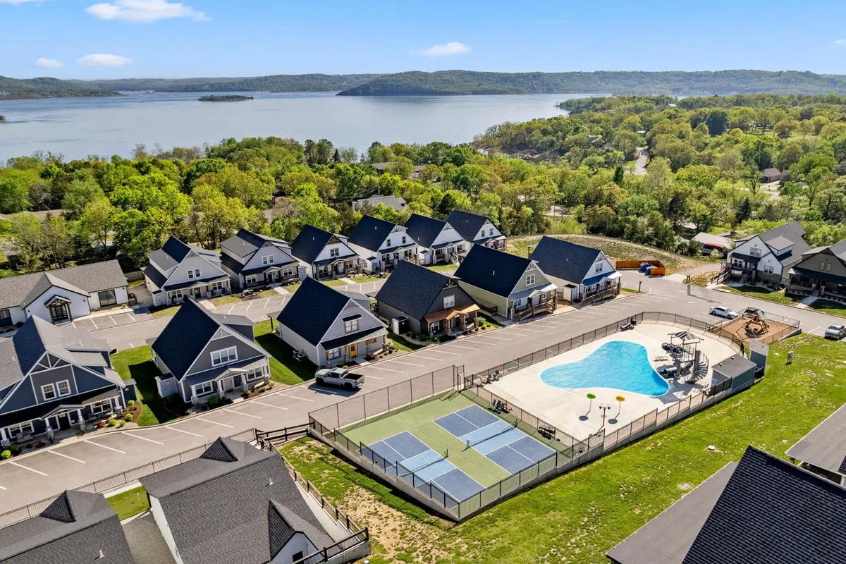 A vibrant exterior view showcasing a swimming pool, tennis courts, well-maintained lawns, and a lake in the background. The setting is active and community-oriented, offering amenities for outdoor recreation and relaxation with scenic views.