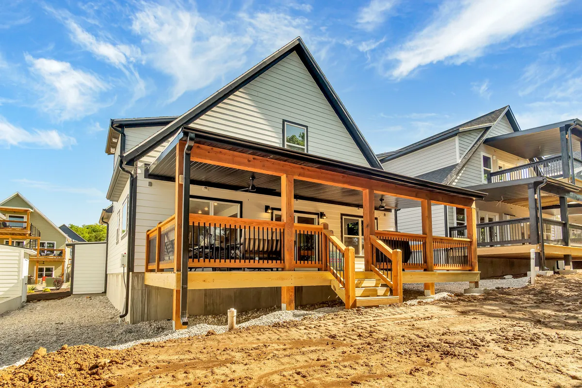A welcoming exterior shot of a wooden deck and cabin facade with exterior walls, roofline details, and a gravel driveway. The deck is ready for outdoor dining, social gatherings, or relaxing after a long day, with the evening light hinting at sunset views.
