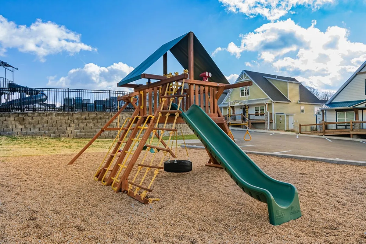 A vibrant outdoor playground structure featuring a slide and a tire swing, surrounded by green space. Children can be seen playing and families are gathered nearby, evoking a lively and joyful atmosphere perfect for children and family gatherings.